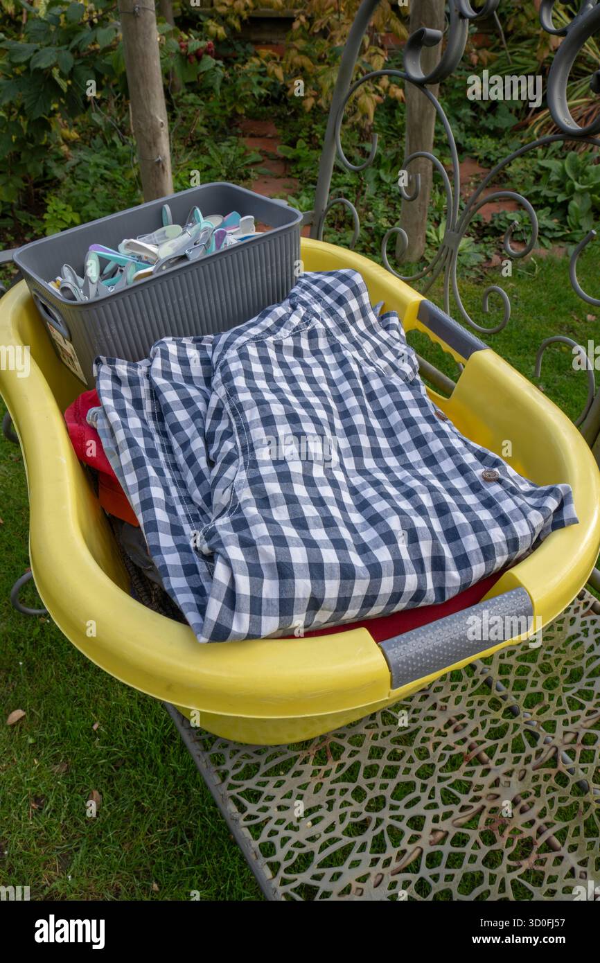 Gelber Wäschekorb mit Kleidung, Heringen und Pfannenbox auf Metallsitzen im Freien Stockfoto