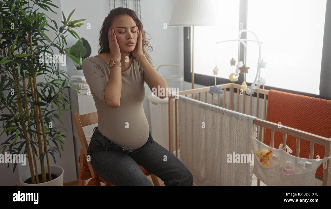 Schwangere Frau, die sich in einem Kinderzimmer unwohl fühlt, umgeben von Babyartikeln, Kinderbett und Pflanzen, die einen intimen Moment in einer Erwartung veranschaulichen Stockfoto