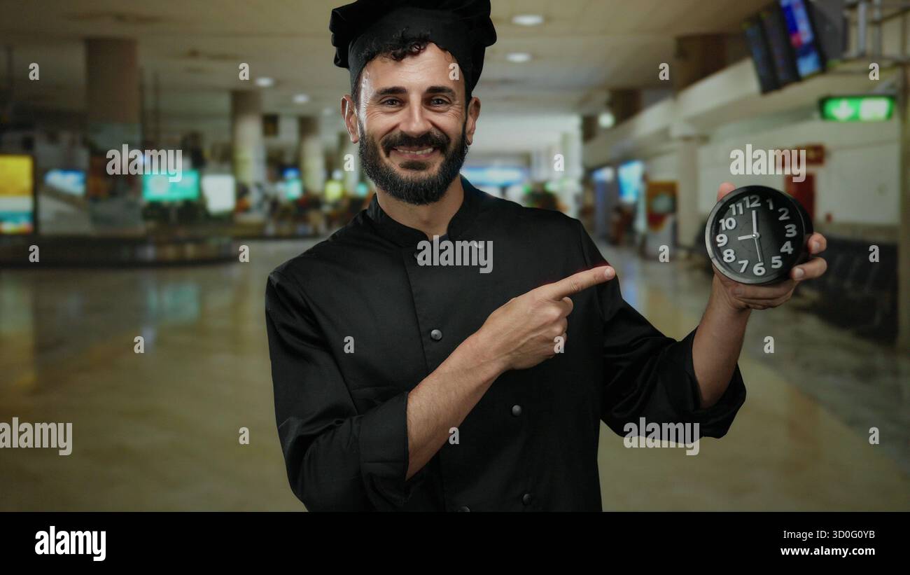 Der hispanische Koch in schwarzer Uniform zeigt auf die Uhr im Flughafenterminal und unterstreicht die Dringlichkeit der Zeit in der geschäftigen Reiseumgebung. Stockfoto