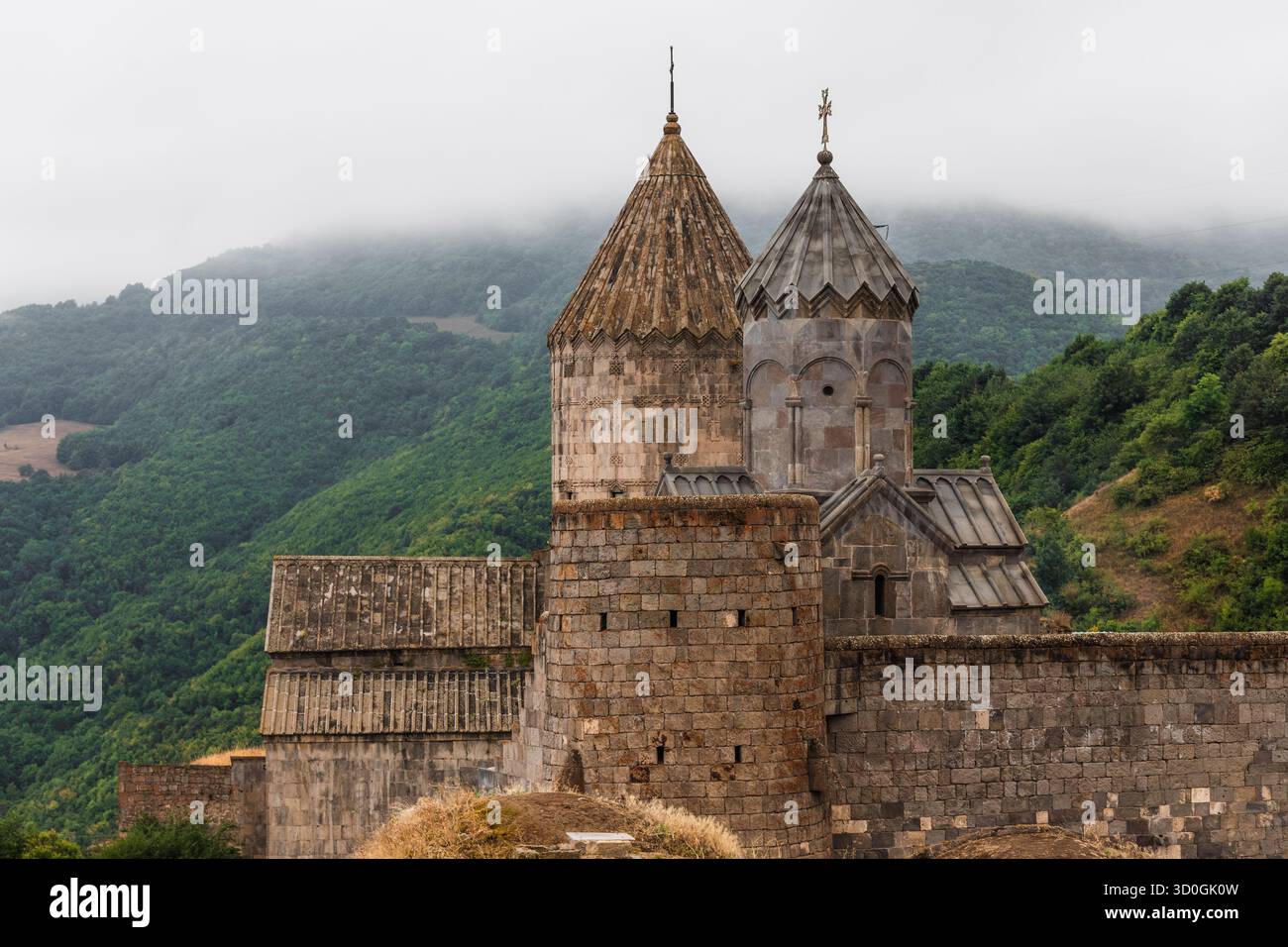 Der Blick auf die antiken Steine des Klosters Tatev erhebt sich vor dem Hintergrund grüner Berge, die in Nebel gehüllt sind, und schafft eine zeitlose Szene, Tatew, Provinz Syunik, Armenien. Stockfoto