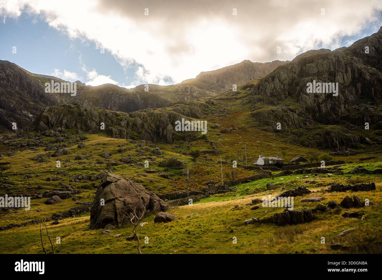 Snowdonia, Wales – 2025.09.21 – Ein einsames Steinhaus befindet sich in einem zerklüfteten Tal unter sonnendurchfluteten Klippen und sanften Hügeln im Snowdonia-Nationalpark. Stockfoto