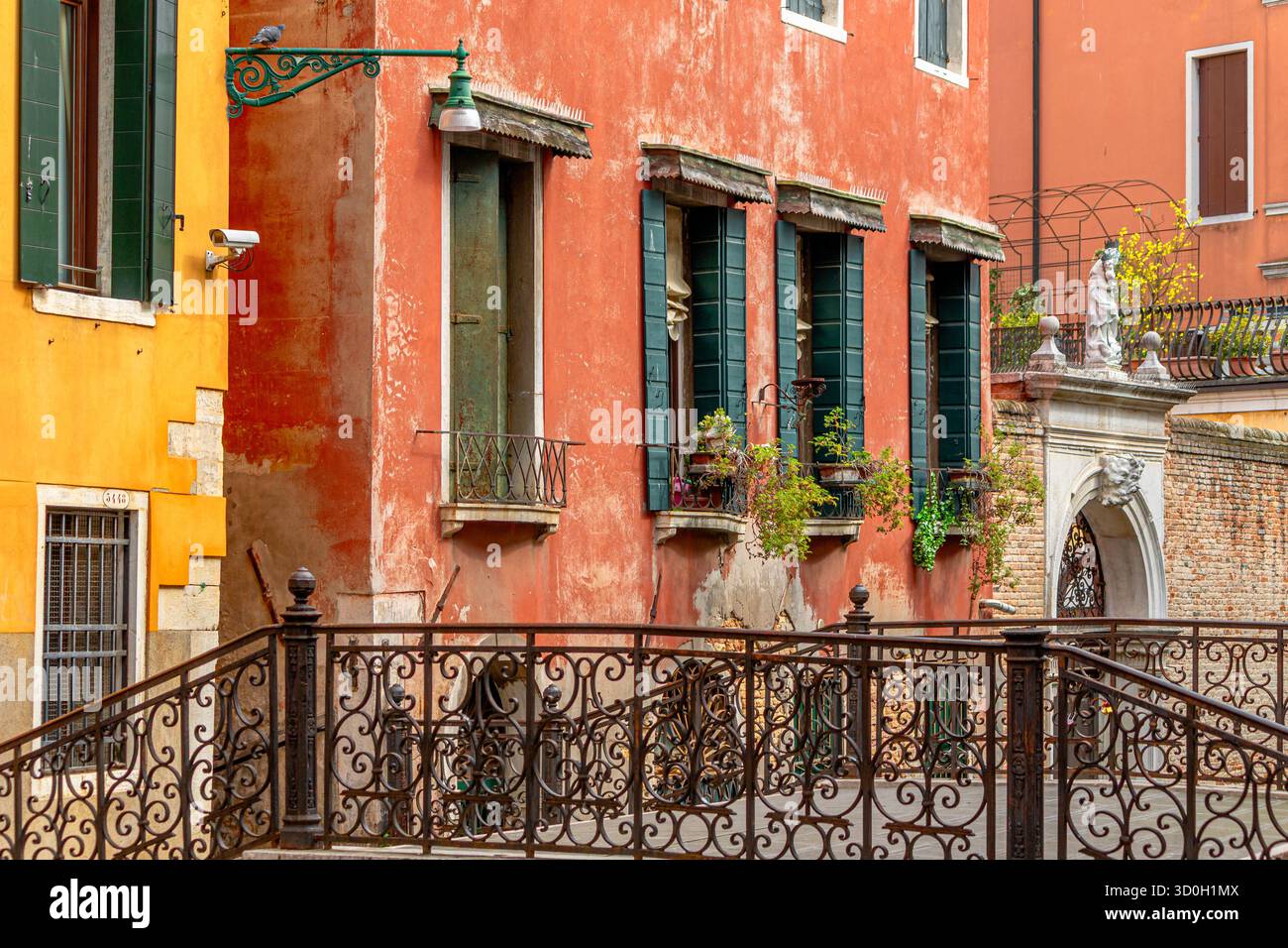 Ein pastellfarbenes Gebäude mit grünen Holzläden in der Nähe einer schmiedeeisernen Kanalbrücke im San Marco Viertel von Venedig Stockfoto