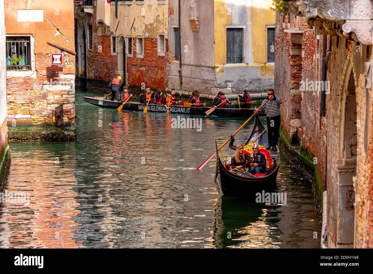 Ein venezianisches Ruderboot fährt hinter einer Gondel vorbei und bringt die Leute auf eine Gondelfahrt auf dem Rio del Mondo Novo, einem Kanal in San Marco, Venedig, Italien Stockfoto