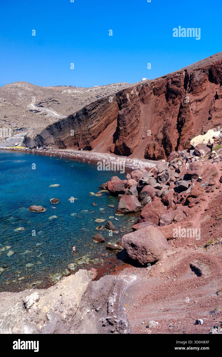 Santorini, GR - 4. September 2025: Der berühmte Rote Strand in Santorin, mit hellrotem vulkanischem Felsen und Sand neben der klaren blauen Ägäis Stockfoto