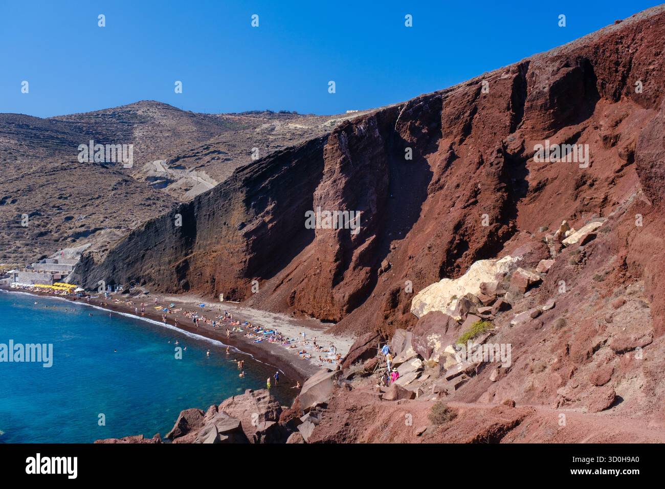 Santorini, GR - 4. September 2025: Der berühmte Rote Strand in Santorin, mit hellrotem vulkanischem Felsen und Sand neben der klaren blauen Ägäis Stockfoto