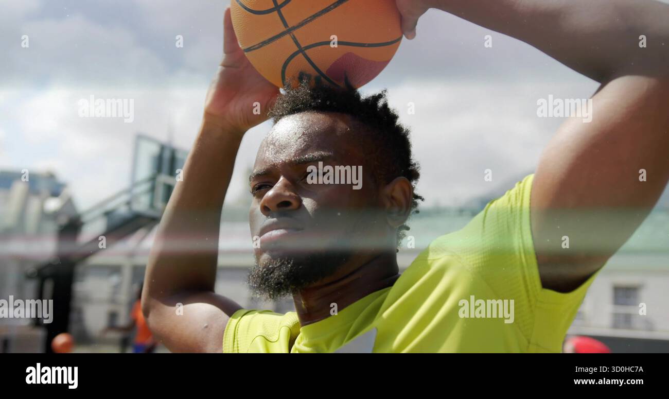 Männlicher Athlet in gelbem Hemd, der Basketball über dem Basketballfeld hält, mit Korb, Rückenbrett Stockfoto