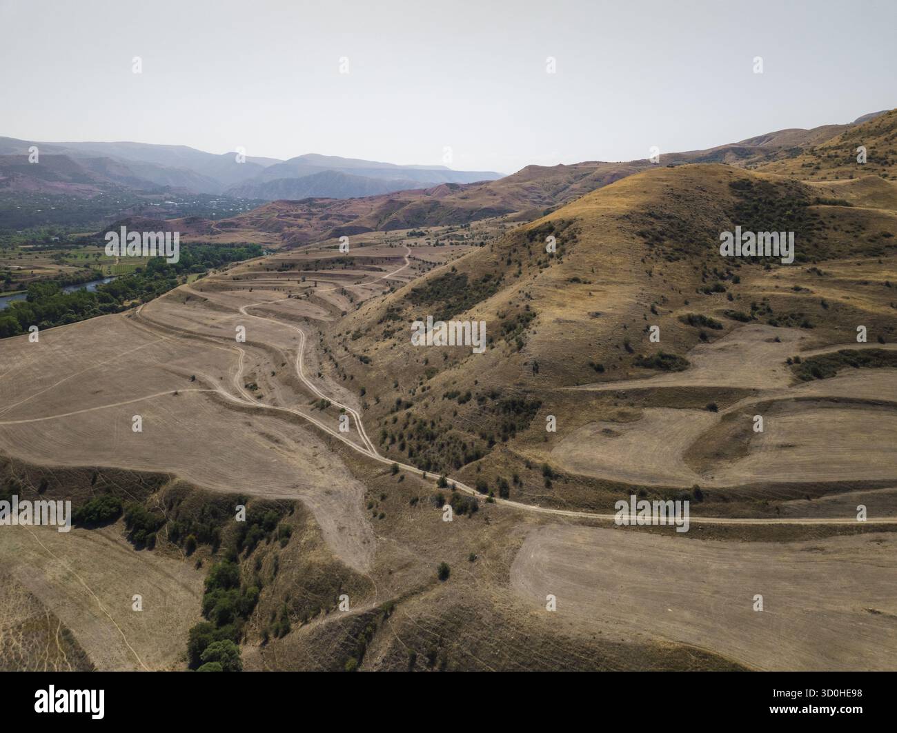 Aus der Vogelperspektive der sonnengebackenen Hügel kaskadieren zum Flussrand, einem Wandteppich aus Erdbraun und gedämpftem Grün, Samtskhe-Javakheti, Samtskhe-Javakh Stockfoto
