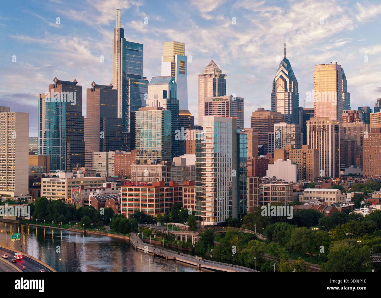 Ein atemberaubender Blick auf die Skyline von Philadelphia, während die Sonne untergeht und ein warmes Leuchten über die Wolkenkratzer wirft. Der Schuylkill River reflektiert die lebendige Farbe Stockfoto