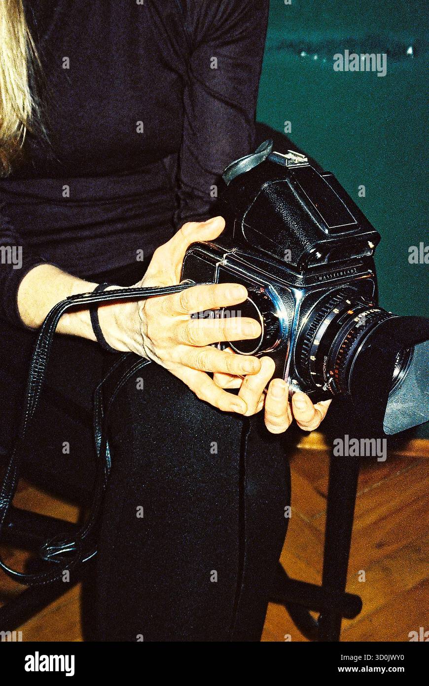Blauhaarige Frau in schwarzer Kleidung mit Hasselblad 500 cm, aufgenommen mit analogem Blitz für einen auffälligen, kontrastreichen Look. Stockfoto
