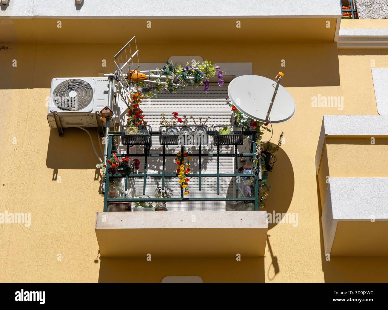 Kleiner Balkon mit Satellitenschüssel, Klimaanlage, terrestrische Antenne, Blumen auf kleinem Raum, geschlossene Fensterläden, in der Stadt Vila Real de Sant Stockfoto
