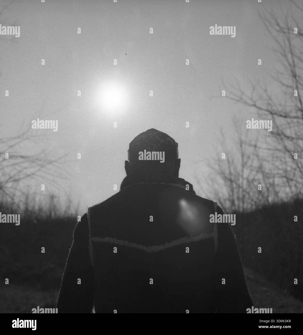 B&W Hasselblad analoges Foto eines älteren Mannes, der auf einer einsamen Uferpromenade unterwegs ist, starke Sonne und Schatten, Sonne, die in die Linse fackelt. Stockfoto