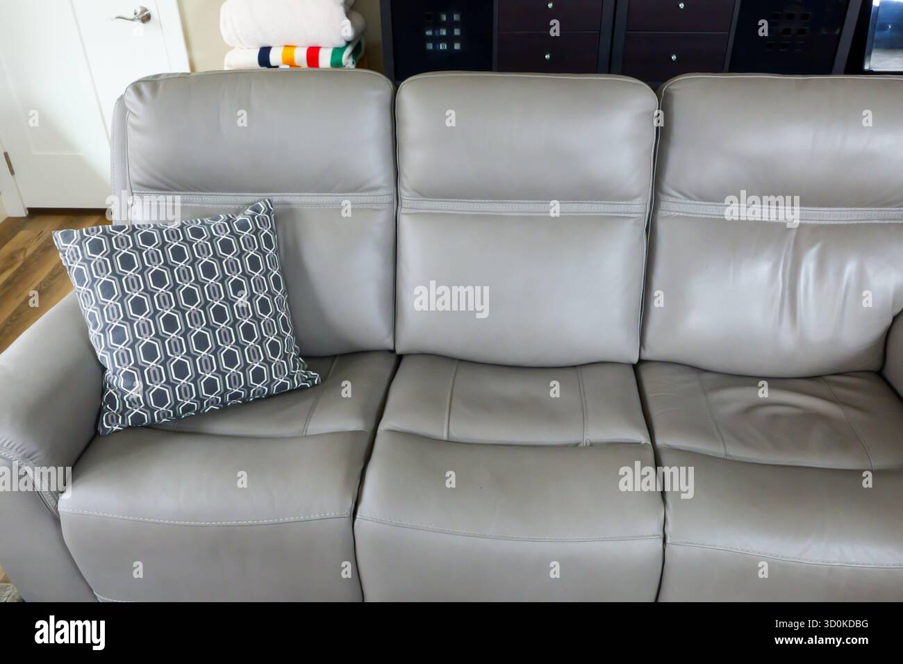 Ein dekoratives Kissen mit grauem Muster am linken Ende eines grauen Sofas in einem Wohnraum. Stockfoto