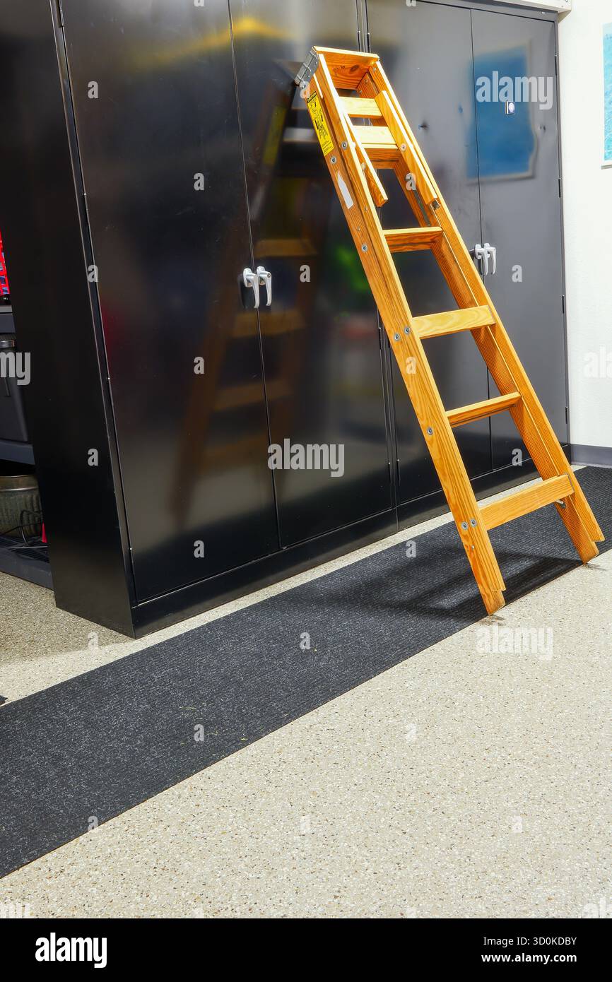 Eine gefaltete Holzleiter oder eine Trittleiter, die an einem schwarzen Schrank in der Garage anlehnt. Stockfoto