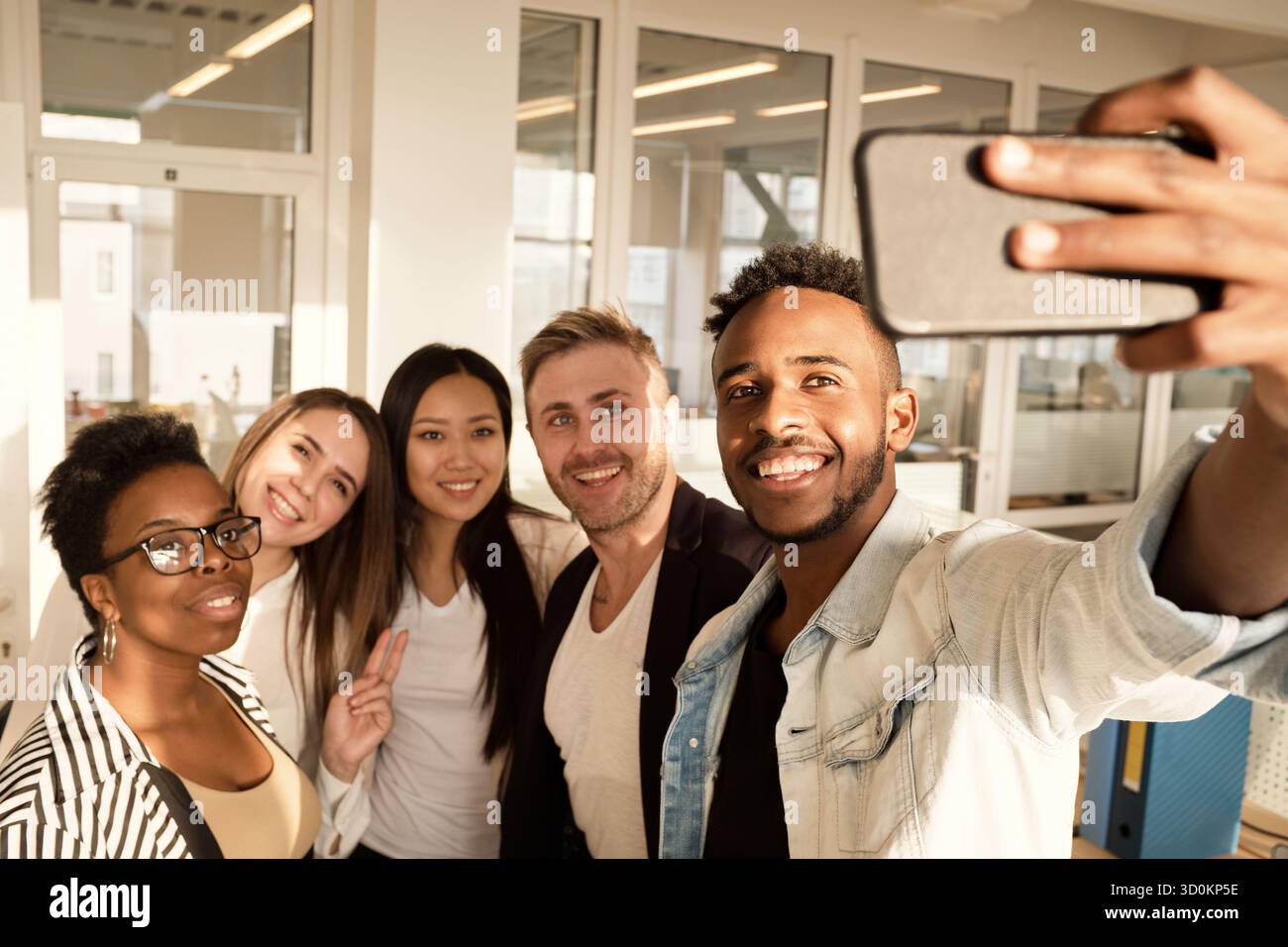 Multiethnische Gruppe junger Kollegen lächelt fröhlich auf die Smartphone-Kamera, während sie im modernen Büro Selfie machen Stockfoto