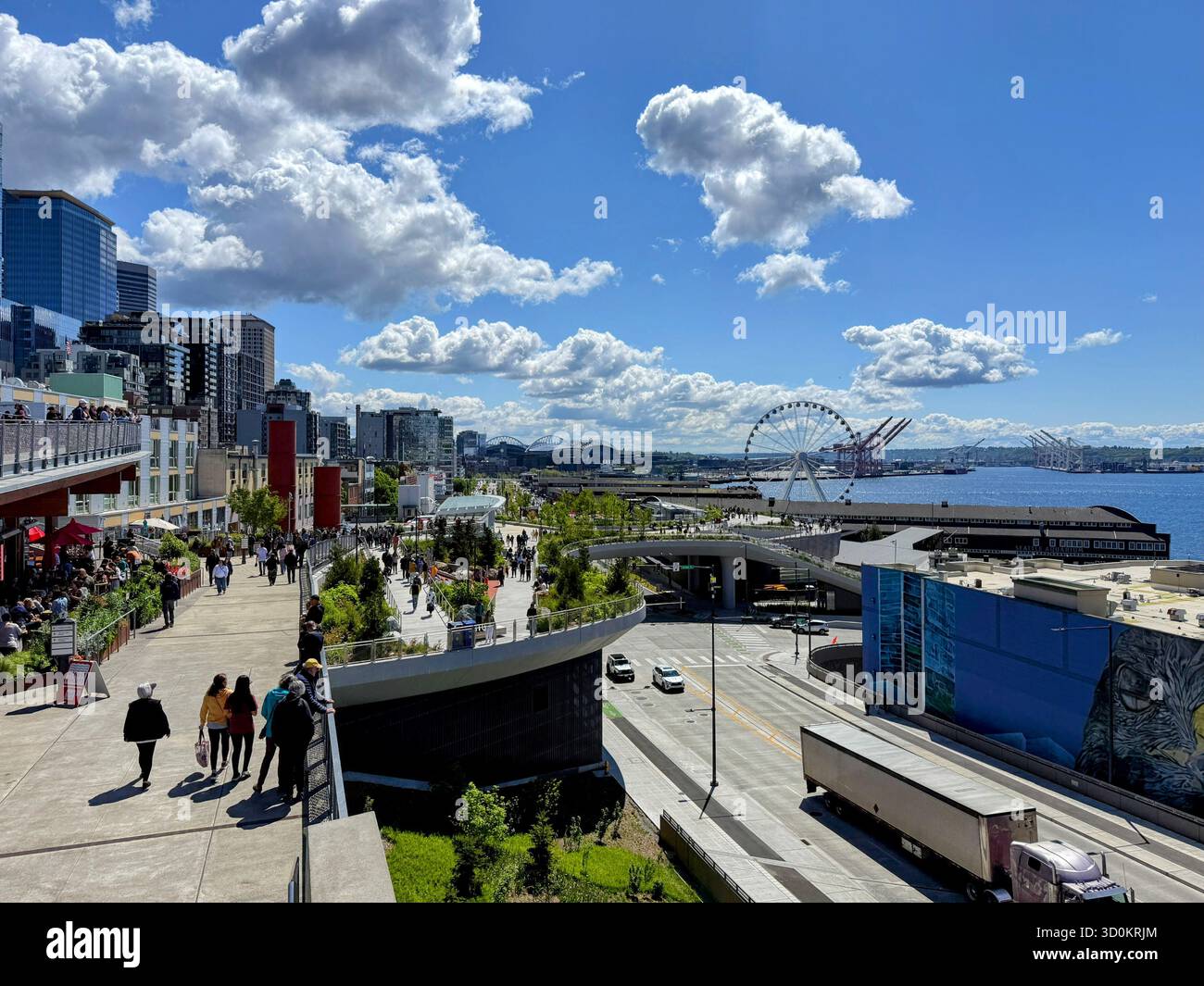 Sonniger Tag im neuen Seattle Waterfront Park, mit Blick auf die Stadt, das Great Wheel, Geschäften und Leuten, die an der Elliott Bay vorbeilaufen. Stockfoto