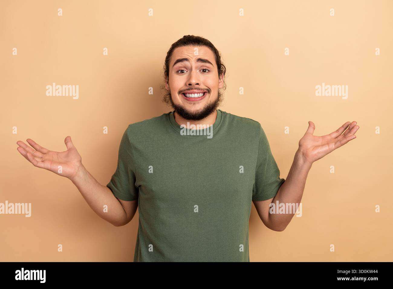 Ein junger Mann mit einem zuckenden und lächelnden Schultern in einem grünen T-Shirt steht vor einem beigen Hintergrund in einem zwanglosen Lifestyle-Werbespot Stockfoto