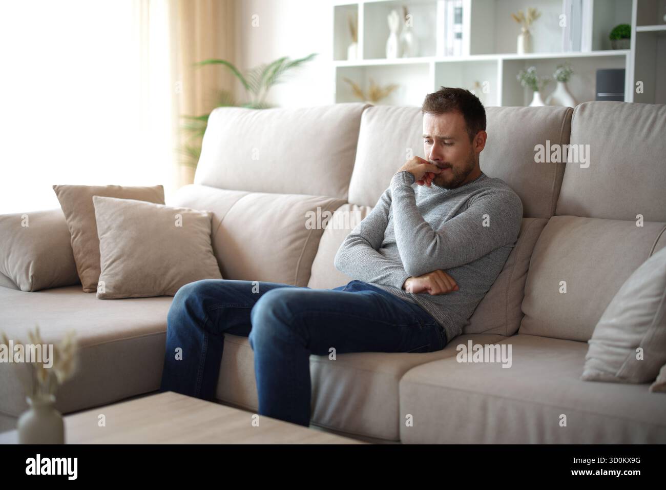 Trauriger Mann, der allein auf einer Couch zu Hause sitzt Stockfoto