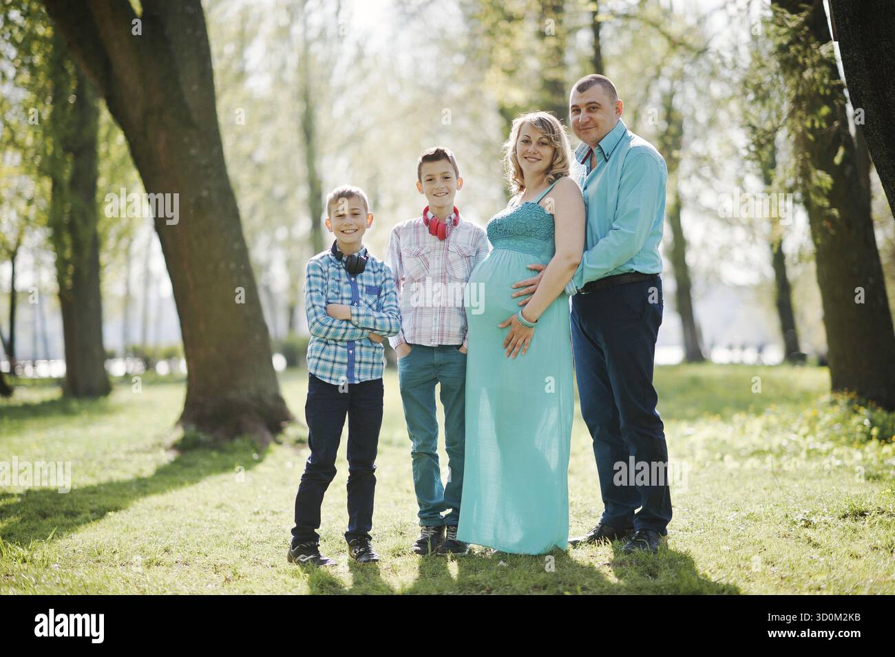 Porträt von glücklich schwanger Familie mit zwei Söhnen, gekleidet in einen türkisfarbenen Kleidern im park Stockfoto