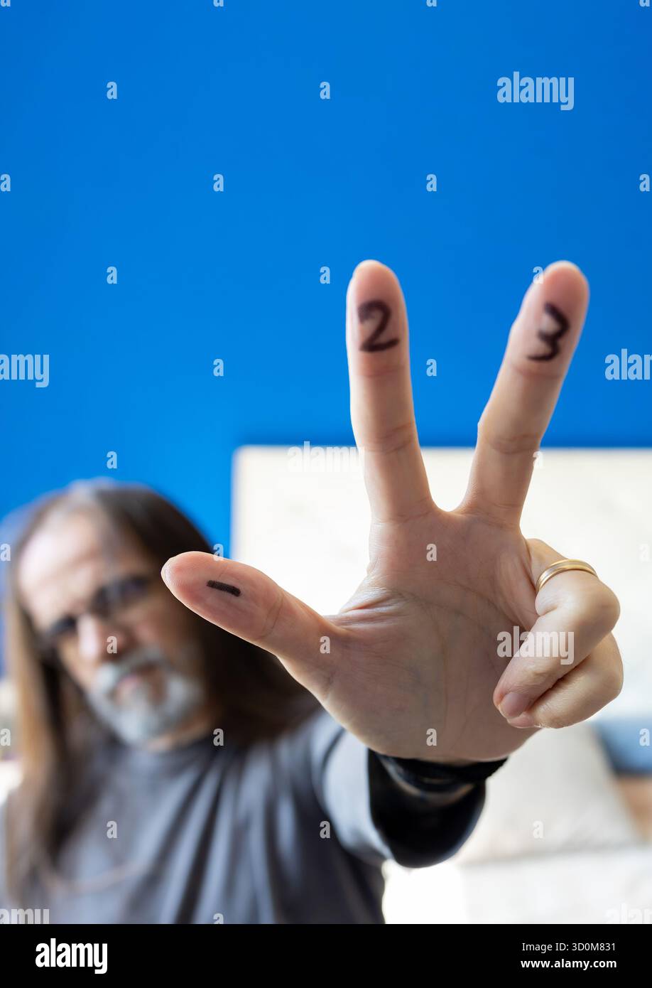 Ein Mann mit Bart und Brille hält seine Hand mit drei gestreckten Fingern hoch. Auf den Fingern sind die Zahlen 1, 2 und 3 eingezeichnet Stockfoto
