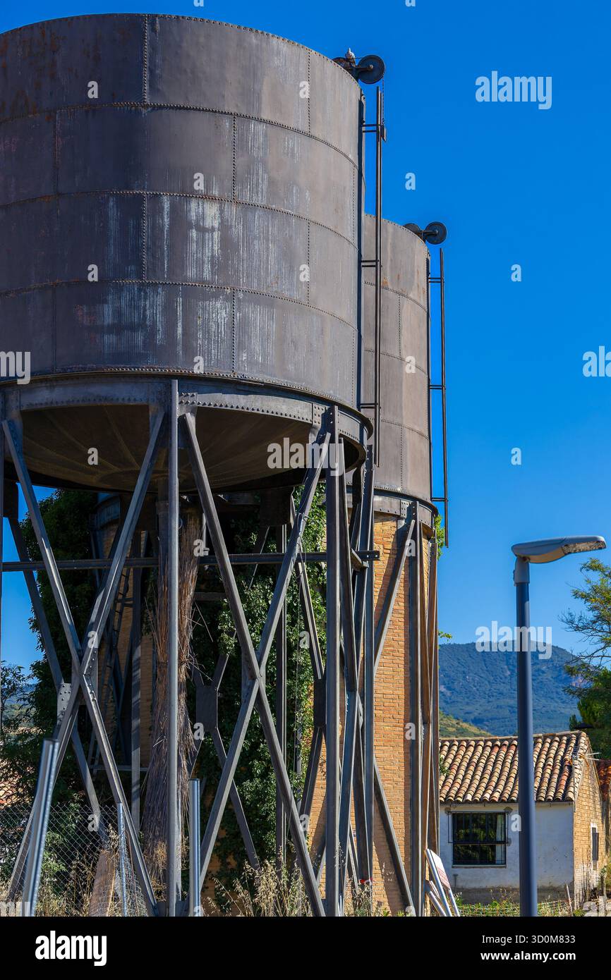 Zwei große Metalltanks. Eine grüne Weinrebe wächst auf einem nahegelegenen Backsteingebäude. Die Tanks sind alt und veraltet Stockfoto