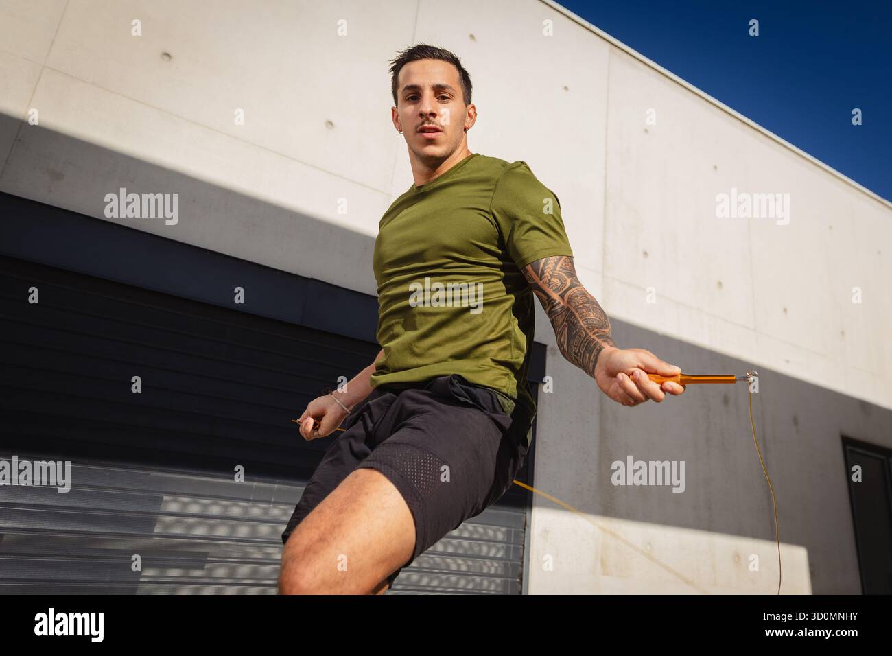 Ein junger, sportlicher Mann, der vor einer Betonwand ein Sprungseiltraining macht. Fotografiert im Sommer unter warmem Licht. Stockfoto