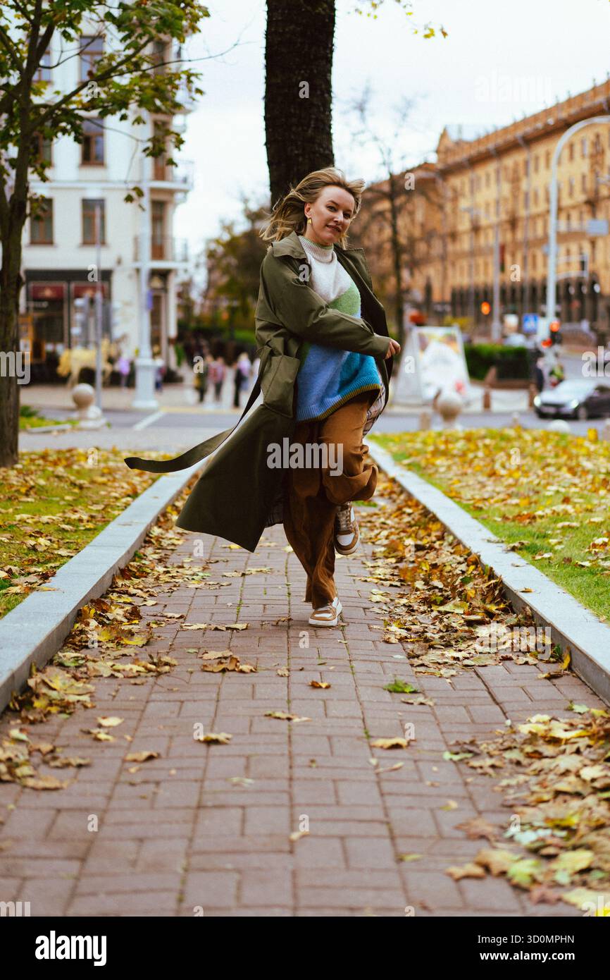Überschwängliche Frau lacht, während sie im Herbst einen Parkweg entlang läuft Stockfoto