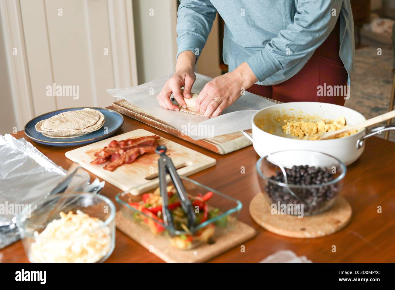 Frau im Yoga-Outfit rollt Frühstücksburrito mit frischen Zutaten Stockfoto