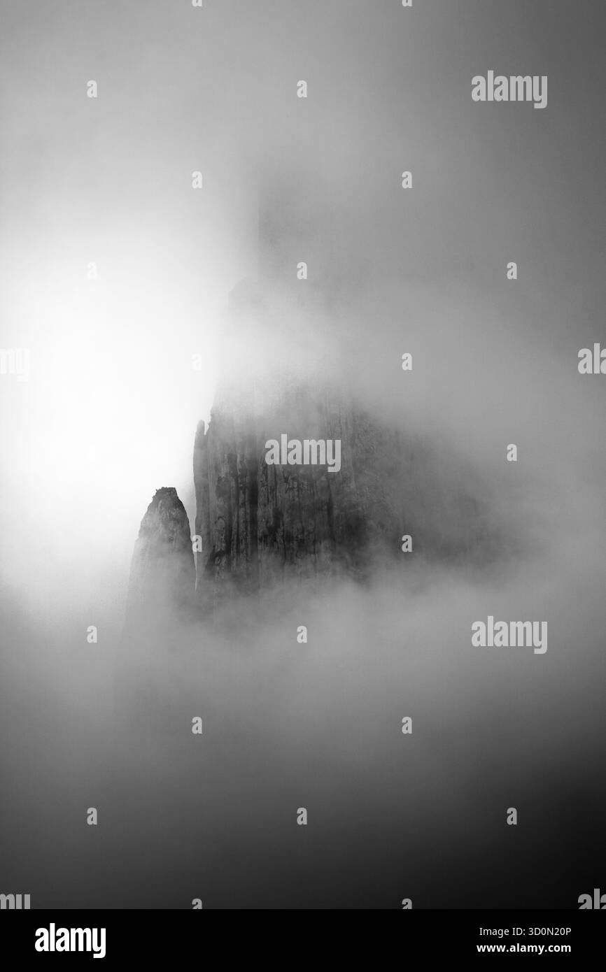 Vertikale Felsformation, umhüllt von Nebel – Schwarzweiß-Foto Stockfoto