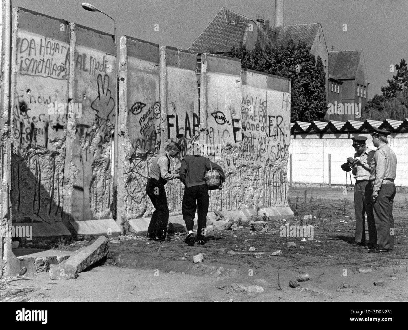 DEU, Deutschland, Berlin, 18.03.1990: Mauerspechte manipulieren die bereits bröckelnde Mauer an der Kiefholzstraße zwischen den Stadtteilen Neukoelln und Treptow. Zwei Mitglieder der DDR-Grenztruppen versuchen, das Geschehen filmisch festzuhalten. [Automatisierte Übersetzung] Stockfoto