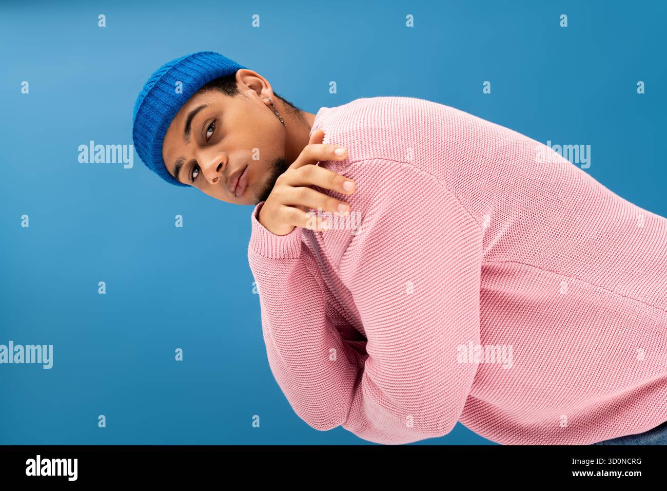 Ein junger Mann in einem pinkfarbenen Pullover und einer blauen Beanie verströmt coole Modeschöpfe. Stockfoto