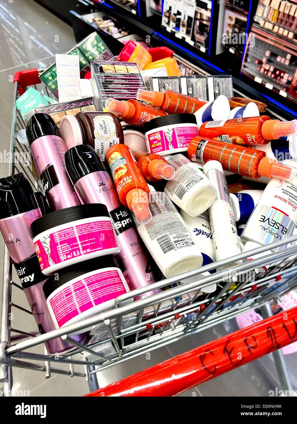 Einkaufswagen überladen mit Kosmetikprodukten in einem Drogerie-Gang, bereit für die Regalpräsentation - Smartphone-aufgenommenes Stockfoto
