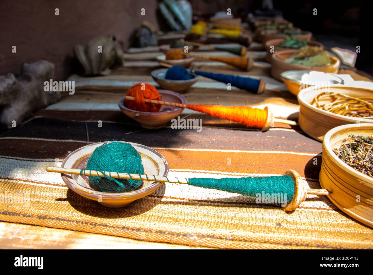 Farbenfrohes handgesponnenes Garn auf Holzspindeln mit natürlichen Farben und Fasern, das traditionelle Textilhandwerkskunst in lebendigem Licht zeigt. Stockfoto