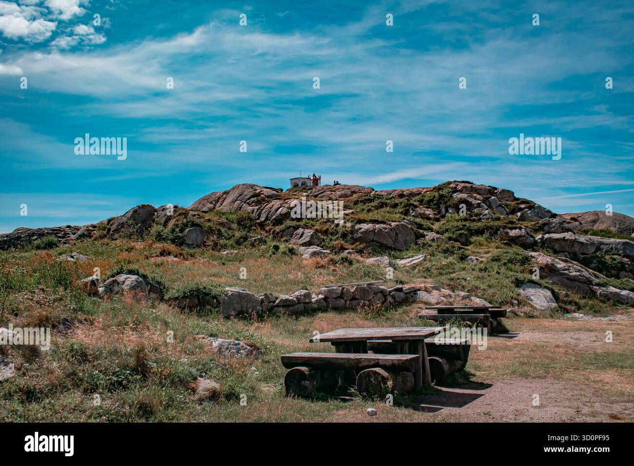 Eine malerische Landschaft mit einem felsigen Hügel, gekrönt von einem kleinen Gebäude mit hölzernen Picknicktischen und -Bänken. Stockfoto