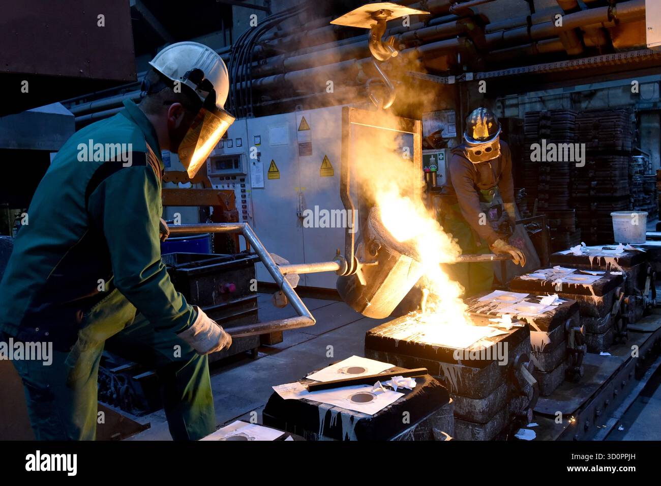 Gruppe von Arbeitnehmern in einer Eisengießerei - Gießen eines Werkstücks mit flüssigem heißem Metall in eine Form - Zusammenarbeit und Arbeitssicherheit - Nahaufnahme Stockfoto