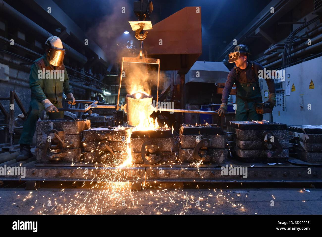 Gruppe von Arbeitnehmern in einer Eisengießerei - Gießen eines Werkstücks mit flüssigem heißem Metall in eine Form - Zusammenarbeit und Arbeitssicherheit - Nahaufnahme Stockfoto