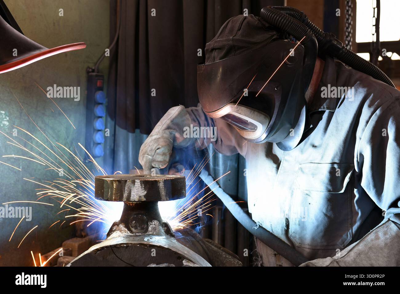 Schweißer in Schutzkleidung am Arbeitsplatz in einem Industrieunternehmen im Stahlbau - Nahaufnahme Stockfoto
