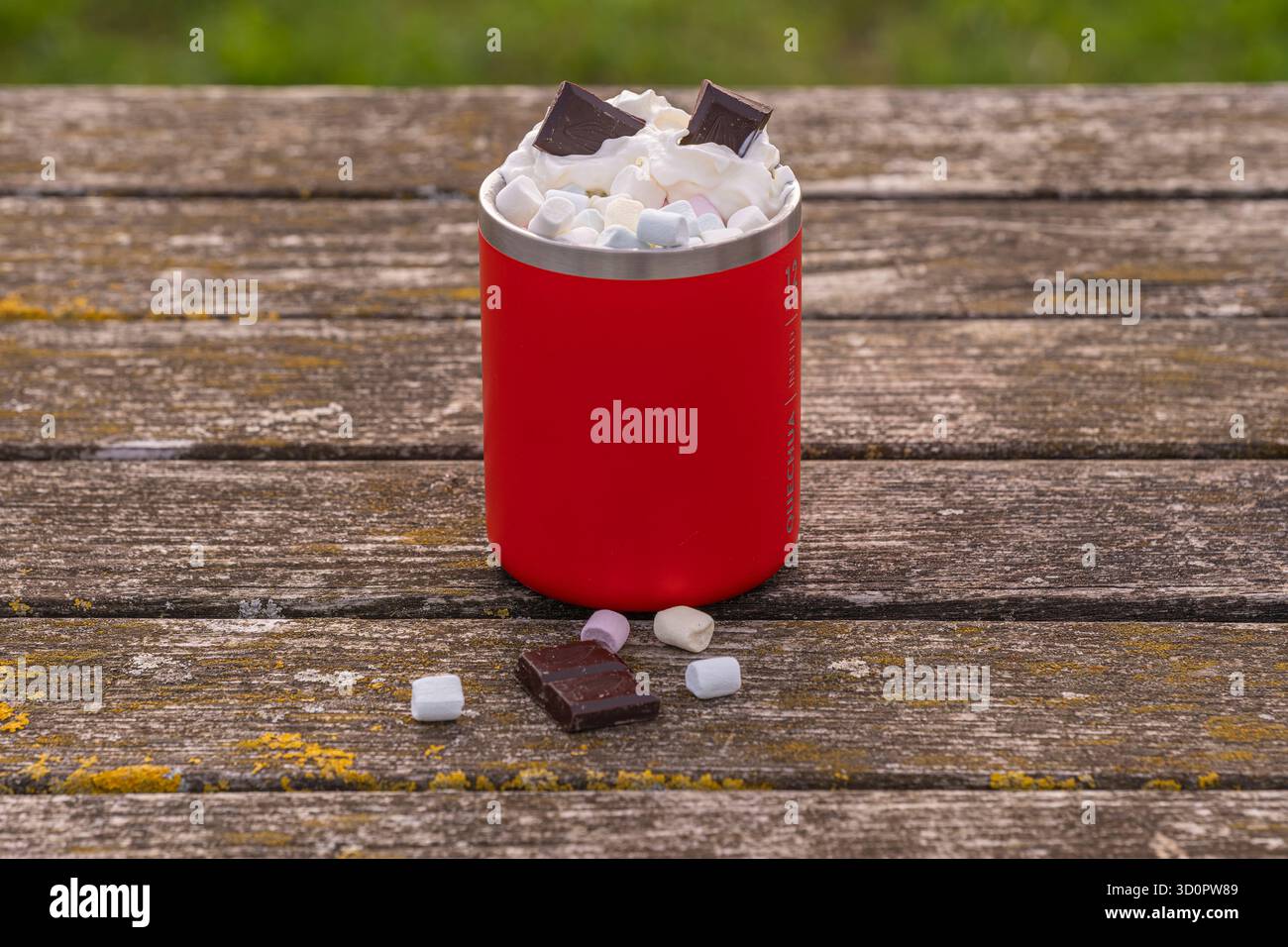 Rote Kaffeetasse mit Schlagsahne, Marshmallow und Schokoladentafeln auf einem alten Holztisch – Seitenansicht Stockfoto
