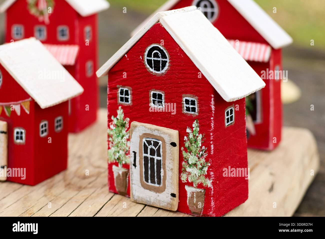 Nahaufnahme bezaubernder roter Miniaturhäuser mit weißen Dächern, festlicher Dekoration und winzigen Topfbäumen, die ein gemütliches Weihnachtsdorf schaffen Stockfoto