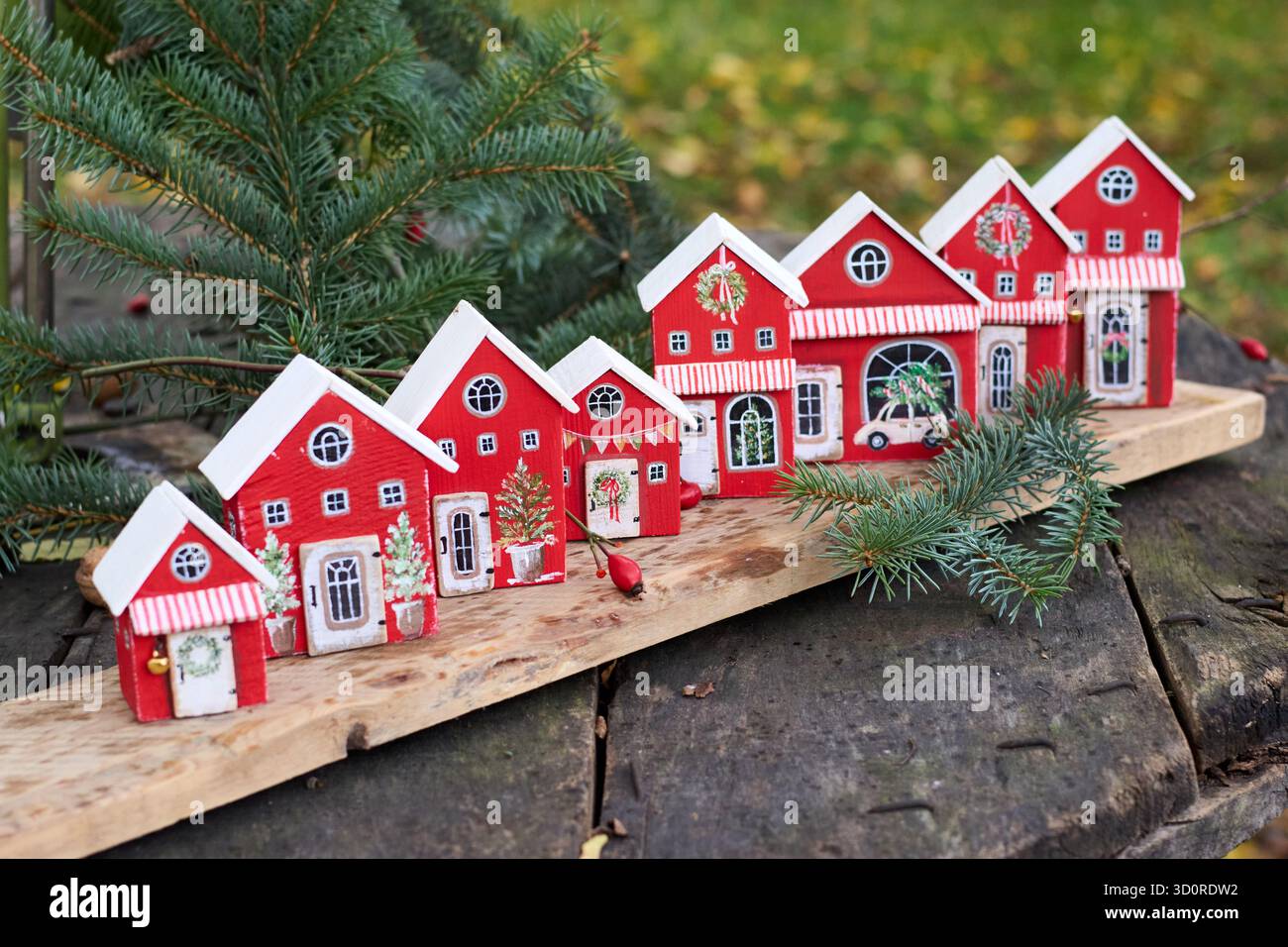 Bezaubernde Reihe roter Weihnachtshäuser mit weißen Dächern und festlichen Dekorationen auf einem Holzbrett schaffen eine skurrile Urlaubsszene. Stockfoto