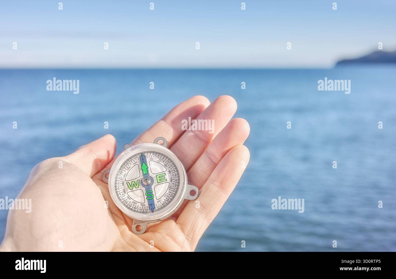Kompass in einer Hand mit Meer im Hintergrund, selektiver Fokus Stockfoto