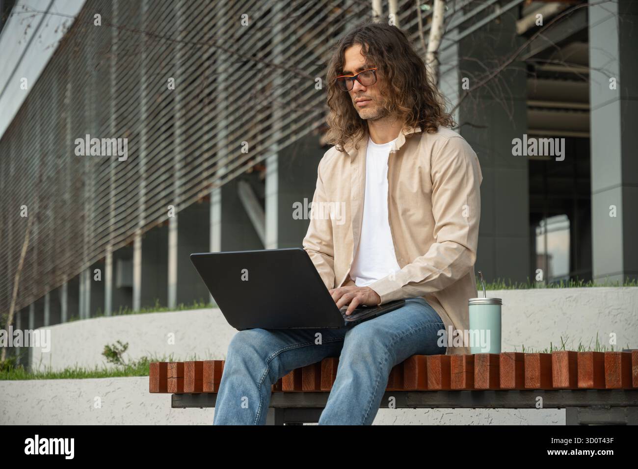 Junger Mann, Student oder Freiberufler sitzt auf der Bank und nutzt einen Laptop für Fernarbeiten im Park. Im Freien. Student genießt die Pause. Stockfoto