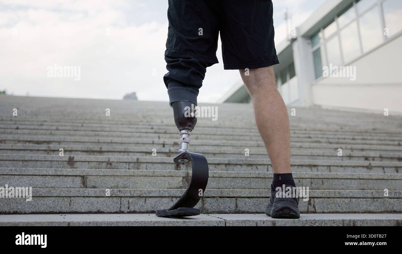 Eine Person mit einer Beinprothese klettert an einem klaren Tag in einem modernen Stadtgebiet Treppen und zeigt Entschlossenheit. Stockfoto