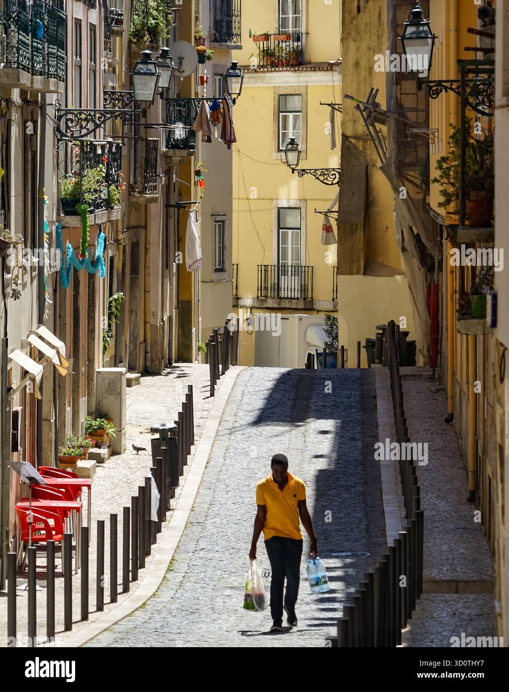 Lissabon, Portugal – Ein Mann, der unter der warmen Nachmittagssonne eine enge Kopfsteinpflasterstraße hinaufläuft. Stockfoto