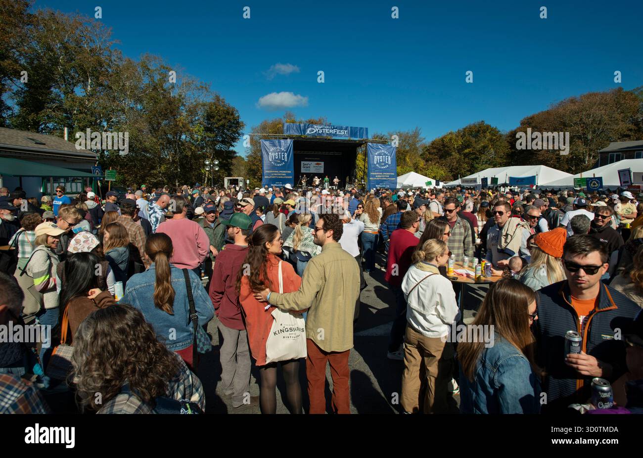 Wellfleet, MA, USA. Oktober 2025. Erster Tag des zweitägigen 25. Jährlichen OysterFest in der kleinen Stadt Cape Cod, 100 Meilen (160 km) auf der Straße südöstlich von Boston, MA. Das von der Wellfleet Oyster Alliance (WOA), einer gemeinnützigen Organisation, die die Muschelindustrie unterstützt, gesponserte Festival zieht über 20.000 Besucher in die kleine Stadt Cape Cod mit einer permanenten Bevölkerung von knapp über 3.500 Menschen an. Foto: Menschenmenge auf dem Parkplatz des Rathauses, während eine Band am ersten Tag des Festivals auf der Bühne spielt. Stockfoto