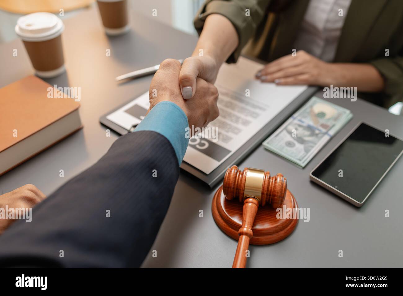 Ein geschäftlicher Handschlag zwischen einem Anwalt und einem Klienten, nachdem er einen Vertrag in einem modernen Büro unterzeichnet hat. Das Abkommen, der Hammer und das Geld auf dem Tisch SY Stockfoto