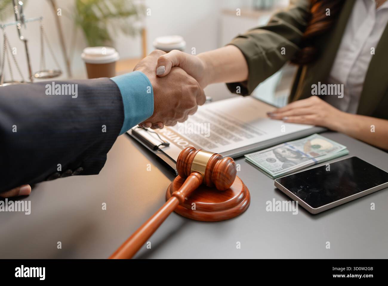Ein geschäftlicher Handschlag zwischen einem Anwalt und einem Klienten, nachdem er einen Vertrag in einem modernen Büro unterzeichnet hat. Das Abkommen, der Hammer und das Geld auf dem Tisch SY Stockfoto