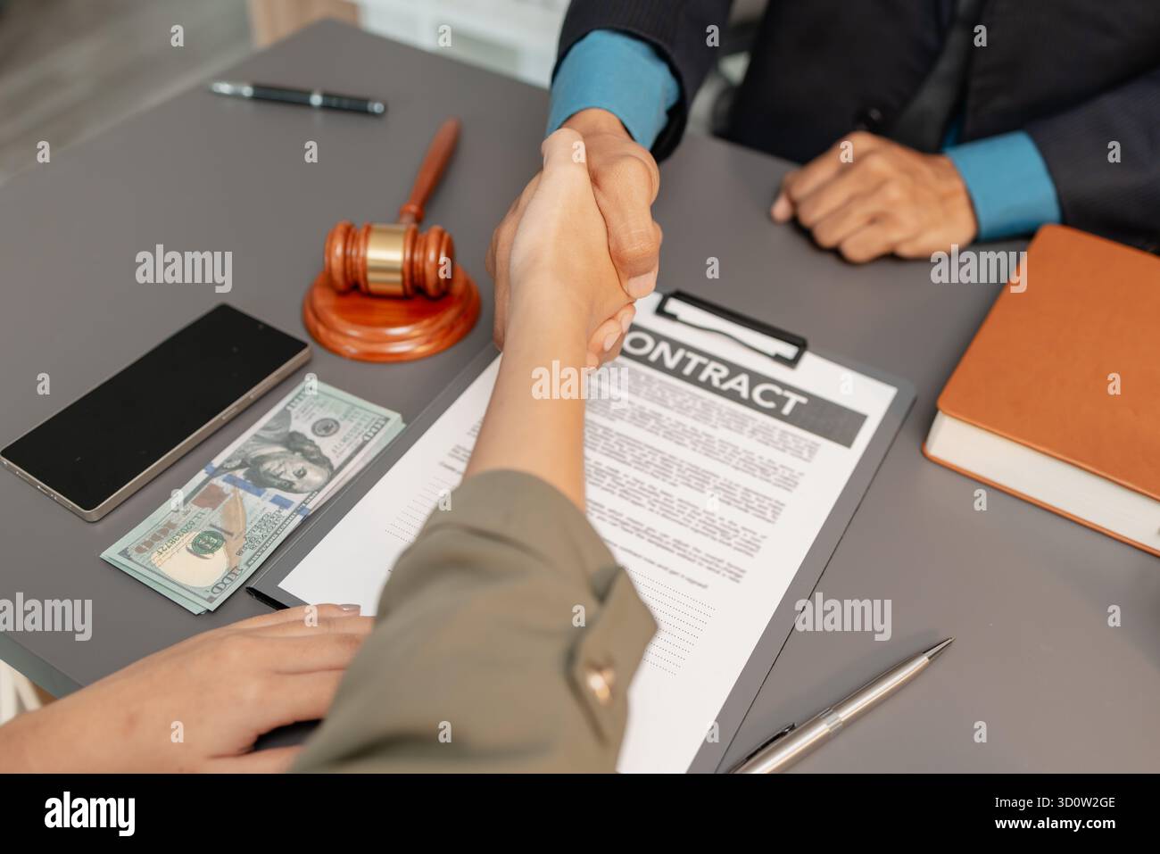 Ein geschäftlicher Handschlag zwischen einem Anwalt und einem Klienten, nachdem er einen Vertrag in einem modernen Büro unterzeichnet hat. Das Abkommen, der Hammer und das Geld auf dem Tisch SY Stockfoto