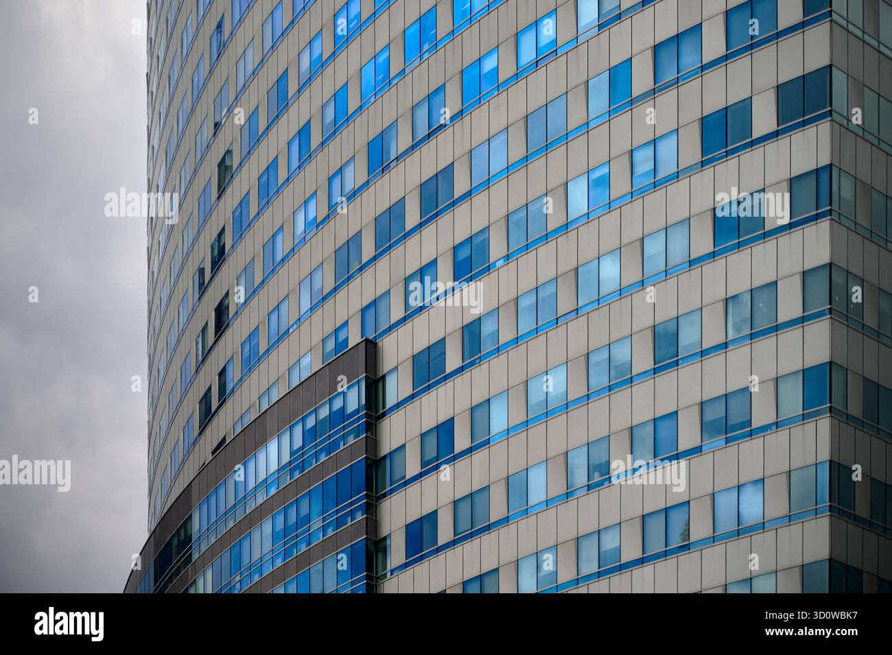 Geschwungene moderne Bürogebäude mit beigefarbener Glasfassade mit blauen Fenstern und markanter abgerundeter Ecke Stockfoto