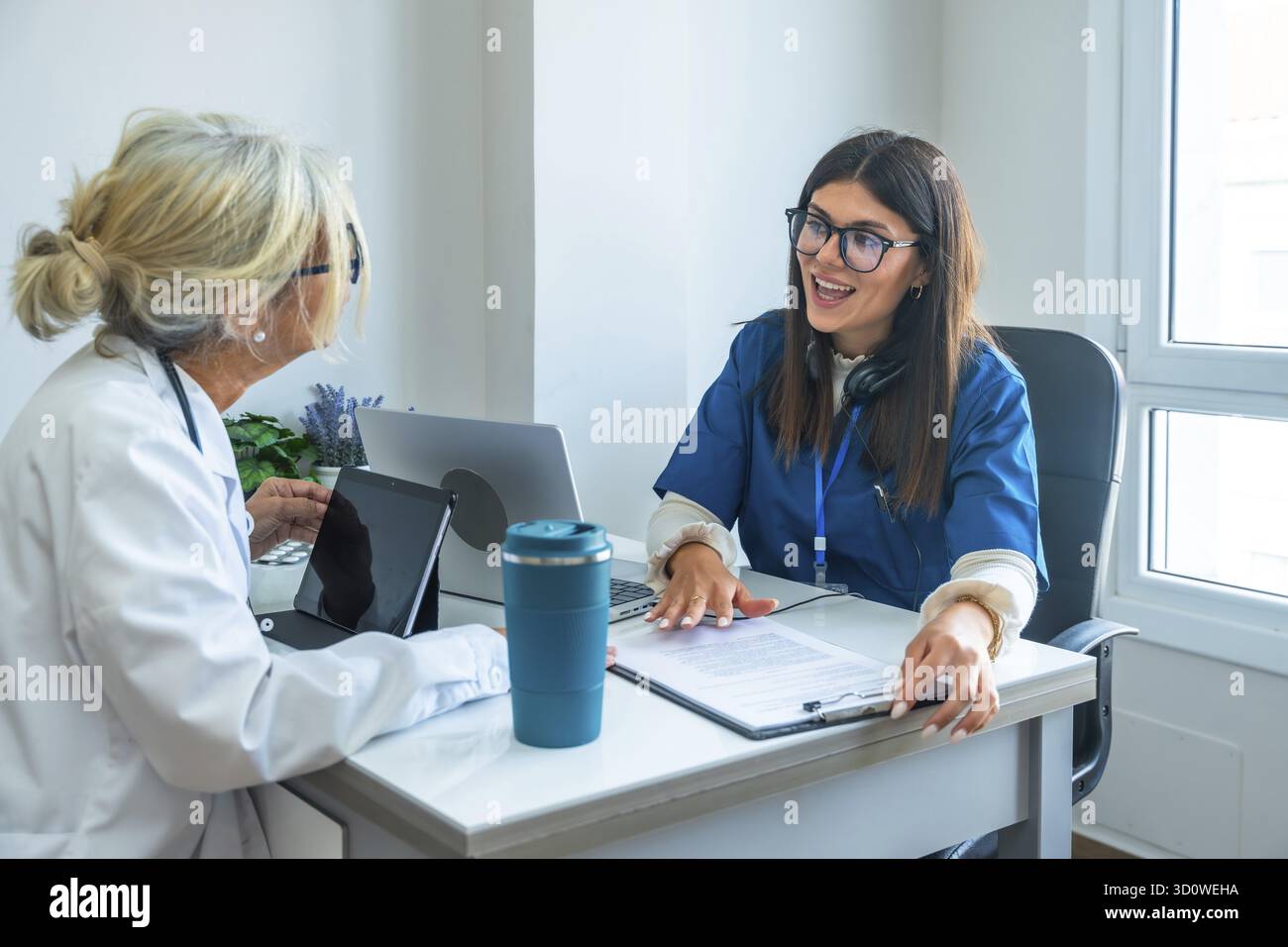 Medizinisches Fachpersonal, ein Arzt im Labormantel und eine Krankenschwester in Peelings, sitzen an einem Schreibtisch und besprechen medizinische Informationen während einer Konsultation usi Stockfoto