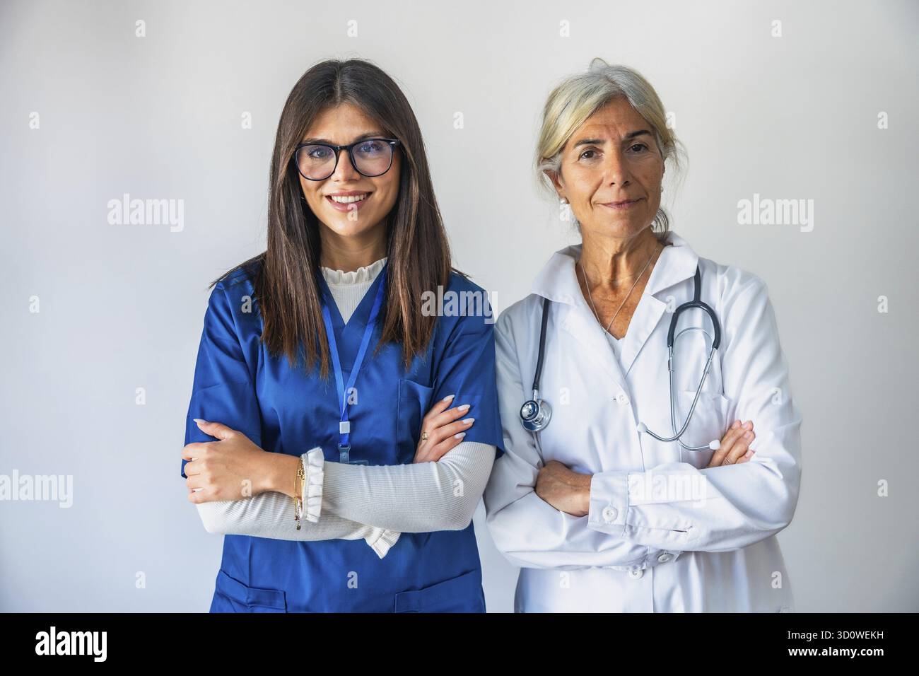 Zwei Frauen im Gesundheitswesen, eine jüngere Krankenschwester in blauen Peelings und ein älterer Arzt in einem weißen Fell mit einem Stethoskop, die selbstbewusst mit f stehen Stockfoto